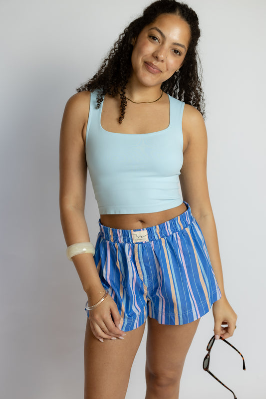 Woman wearing a light blue tank top and blue striped shorts against a white background