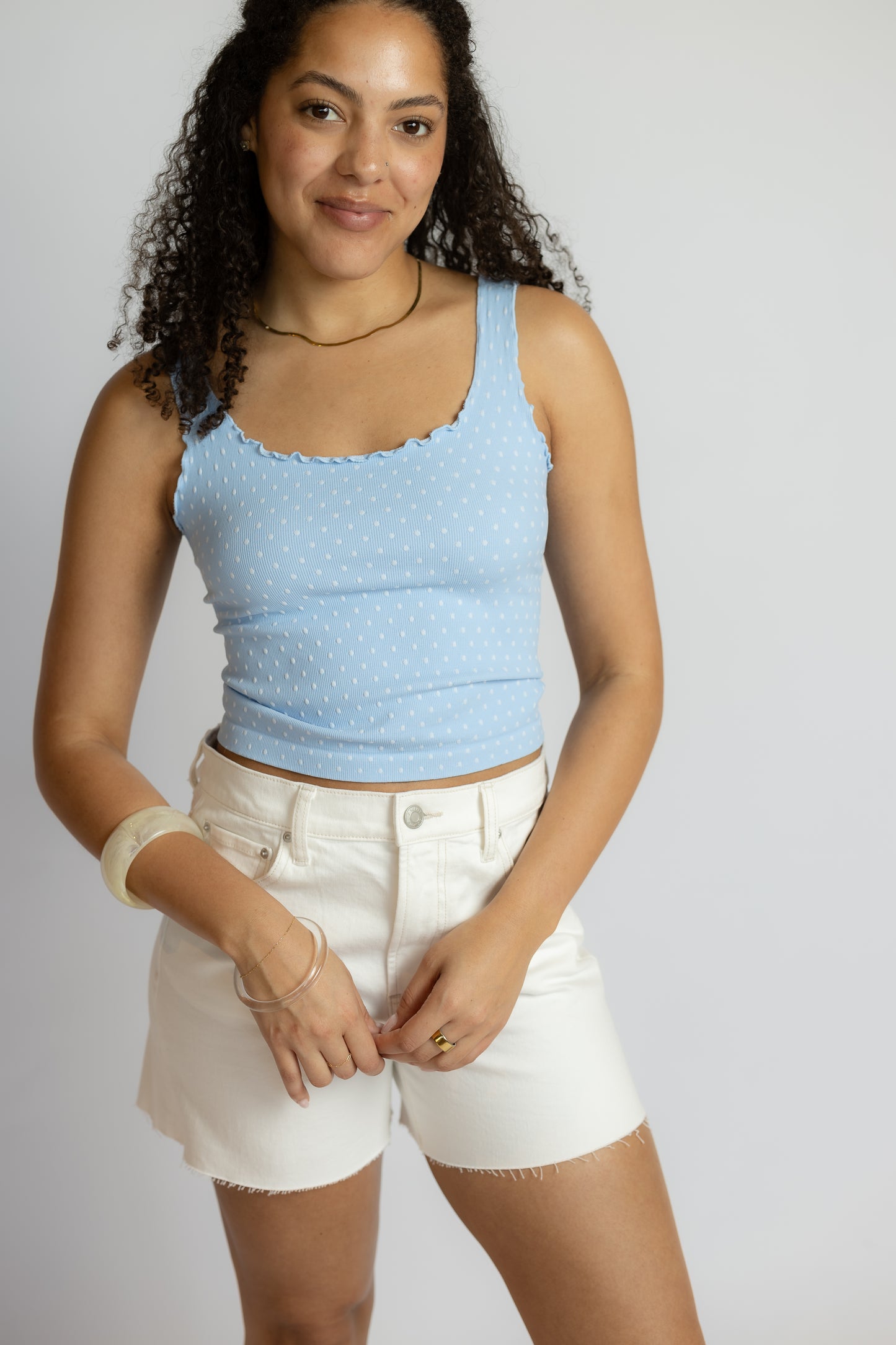 Woman wearing a light blue tank top and white shorts on a plain background