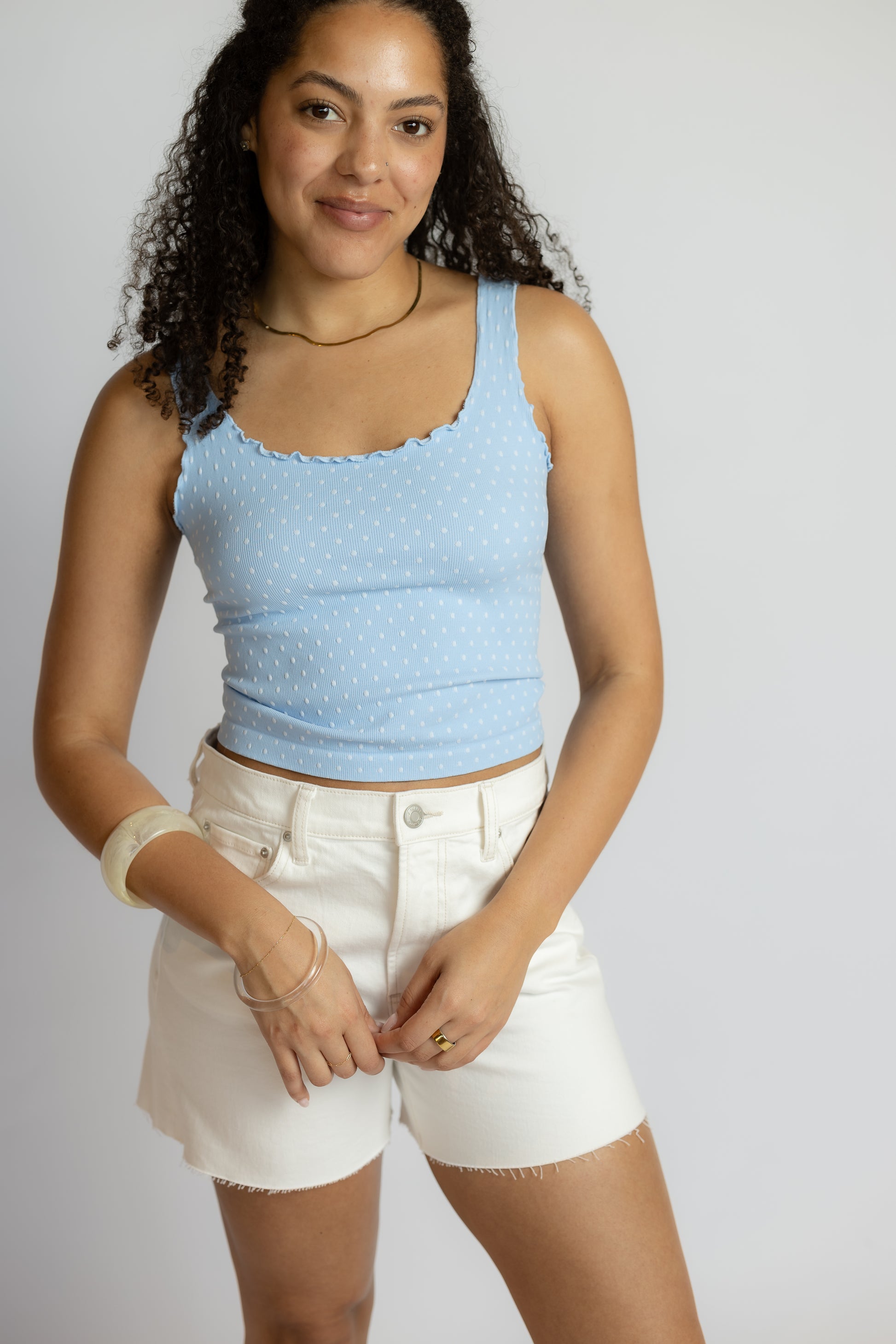 Woman wearing a light blue tank top and white shorts on a plain background