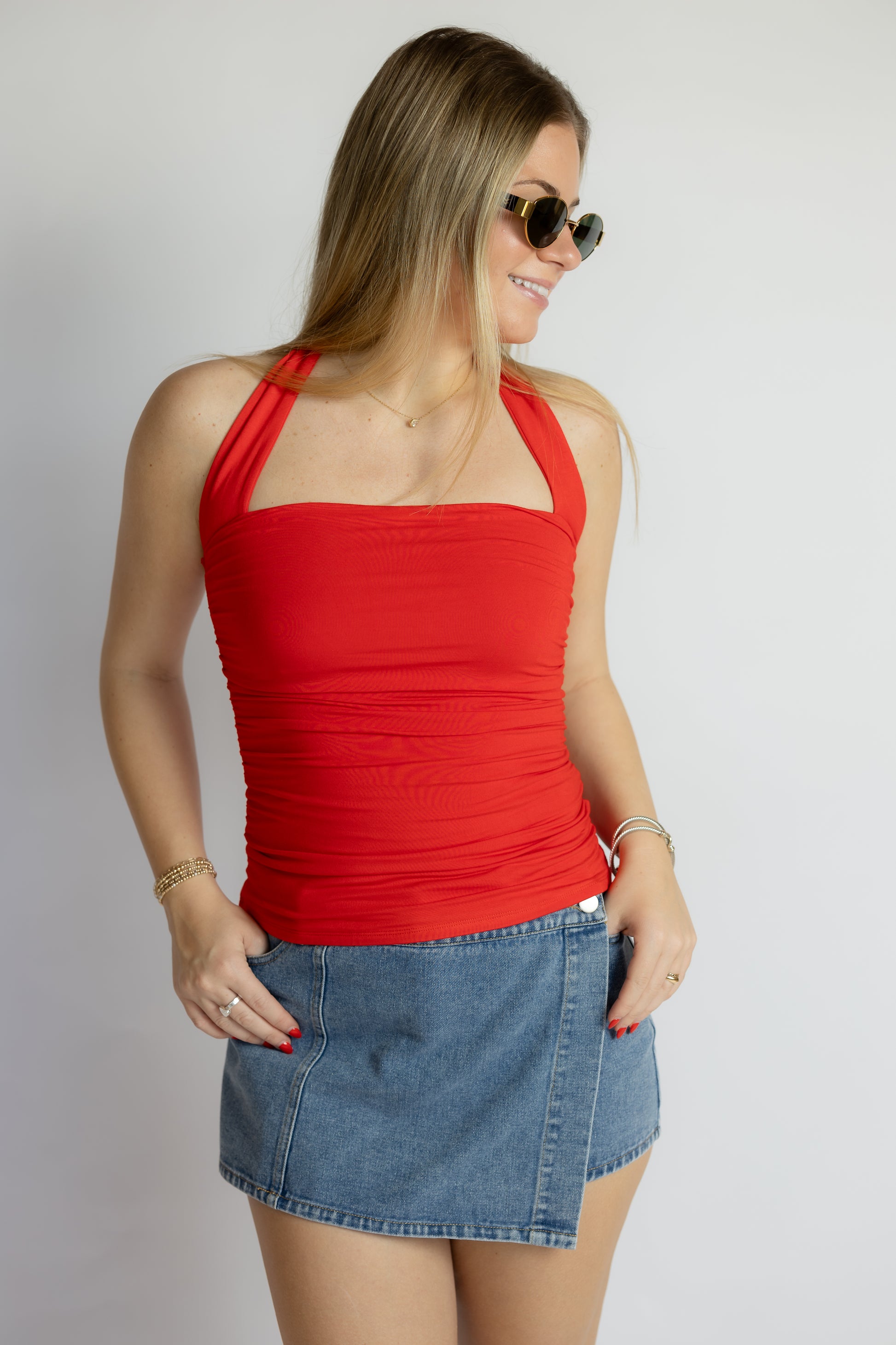Woman wearing a red halter top and denim skirt on a plain background