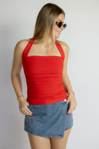 Woman wearing a red halter top and denim skirt on a plain background