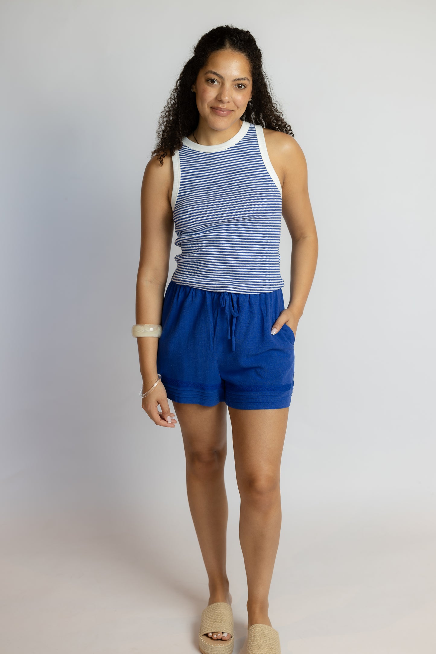 Woman wearing a blue and white striped sleeveless top and blue shorts on a plain background