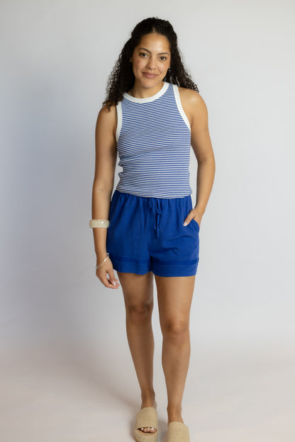 Woman wearing a blue and white striped sleeveless top and blue shorts on a plain background