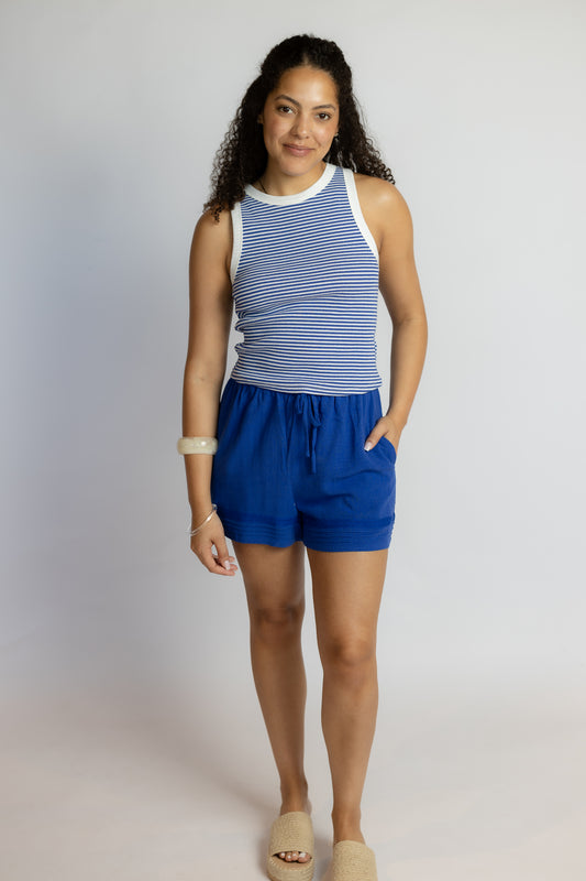 Woman wearing a blue and white striped sleeveless top and blue shorts on a plain background