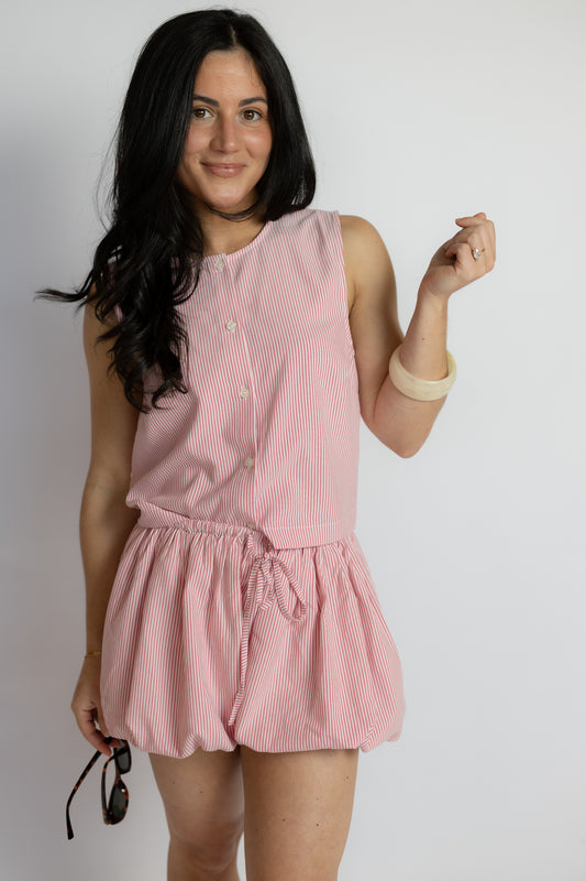 Woman wearing a pink sleeveless top and shorts on a plain background