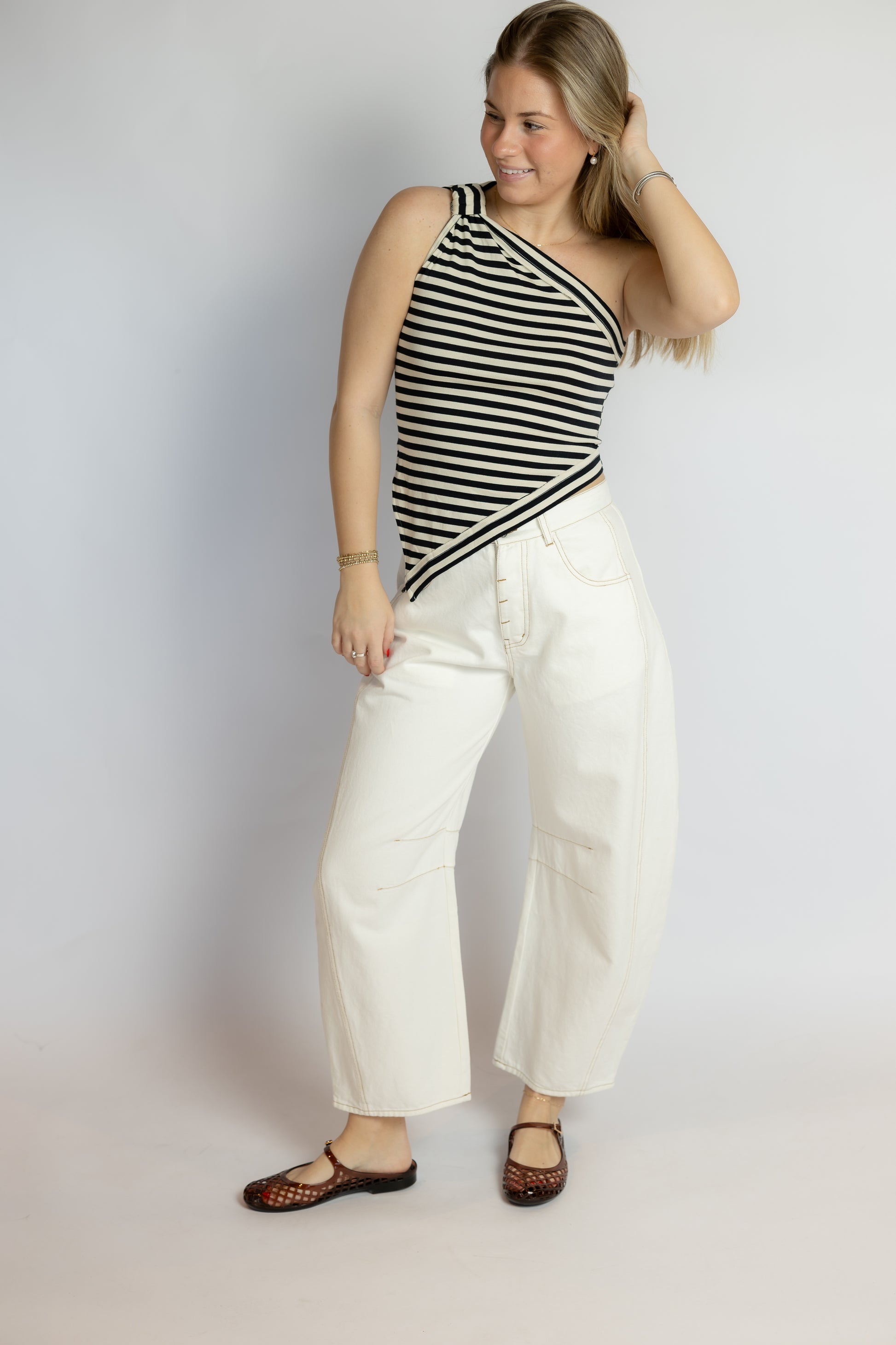 Woman wearing a black and white striped tank top and white pants against a plain background