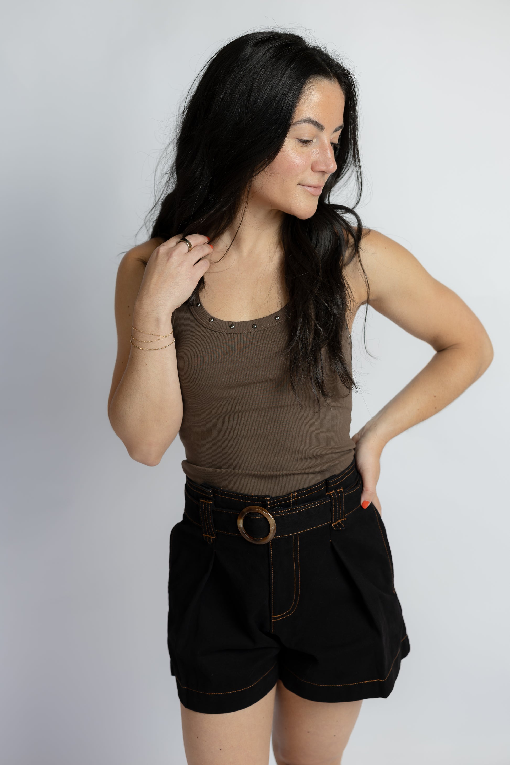 A woman modeling a sleeveless brown tank top and black shorts with a brown belt, photographed against a plain light gray studio background.