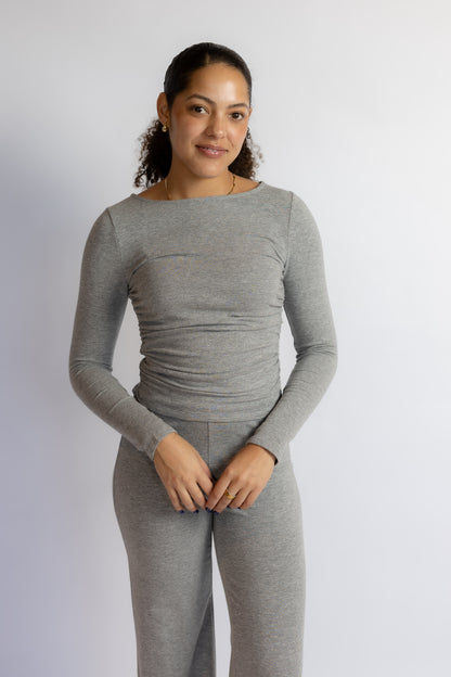 A woman modeling a light gray long-sleeve top and matching gray pants against a plain light gray studio background.