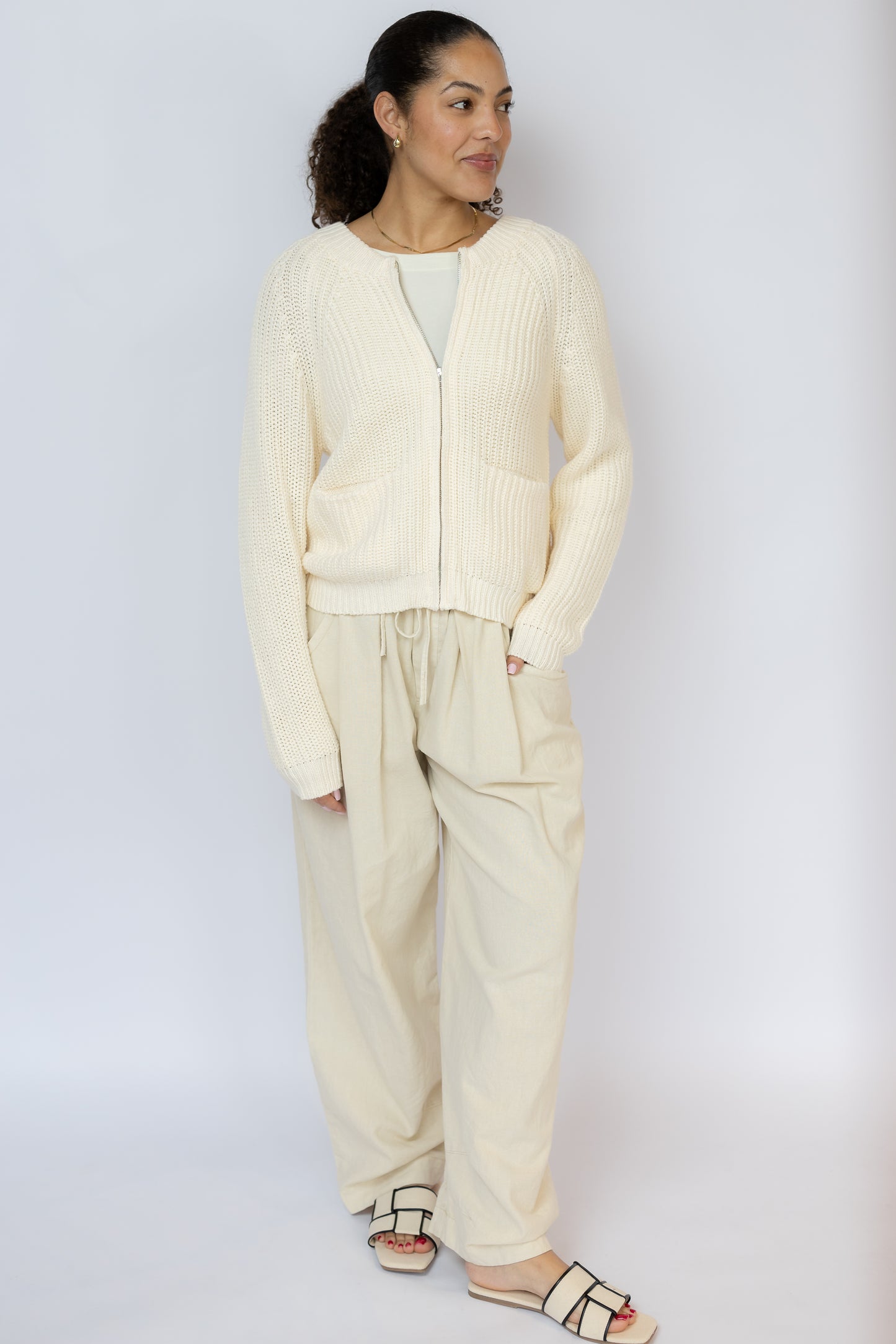 Woman wearing a cream-colored cardigan and pants against a white background