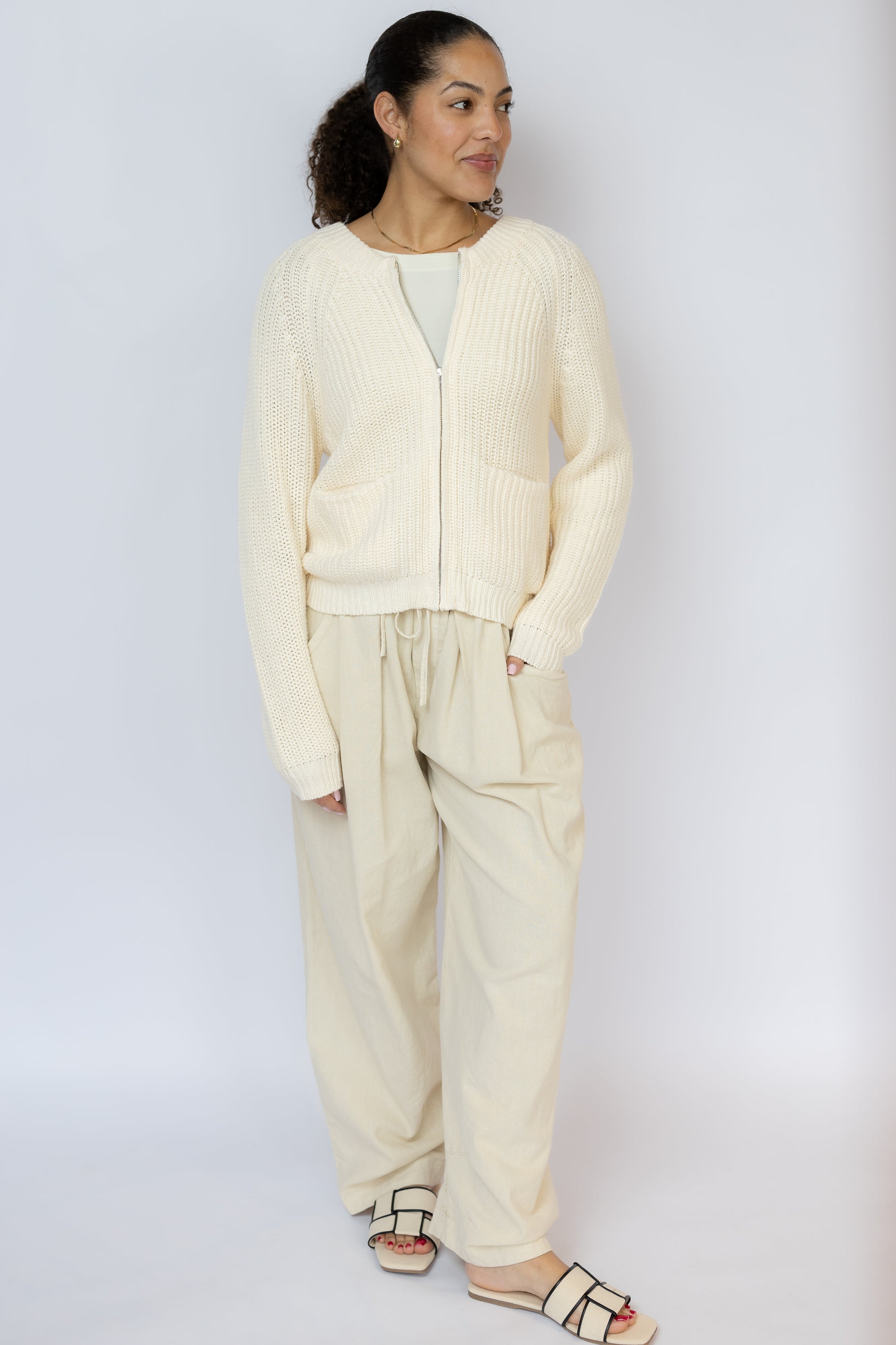 Woman wearing a cream-colored cardigan and pants against a white background