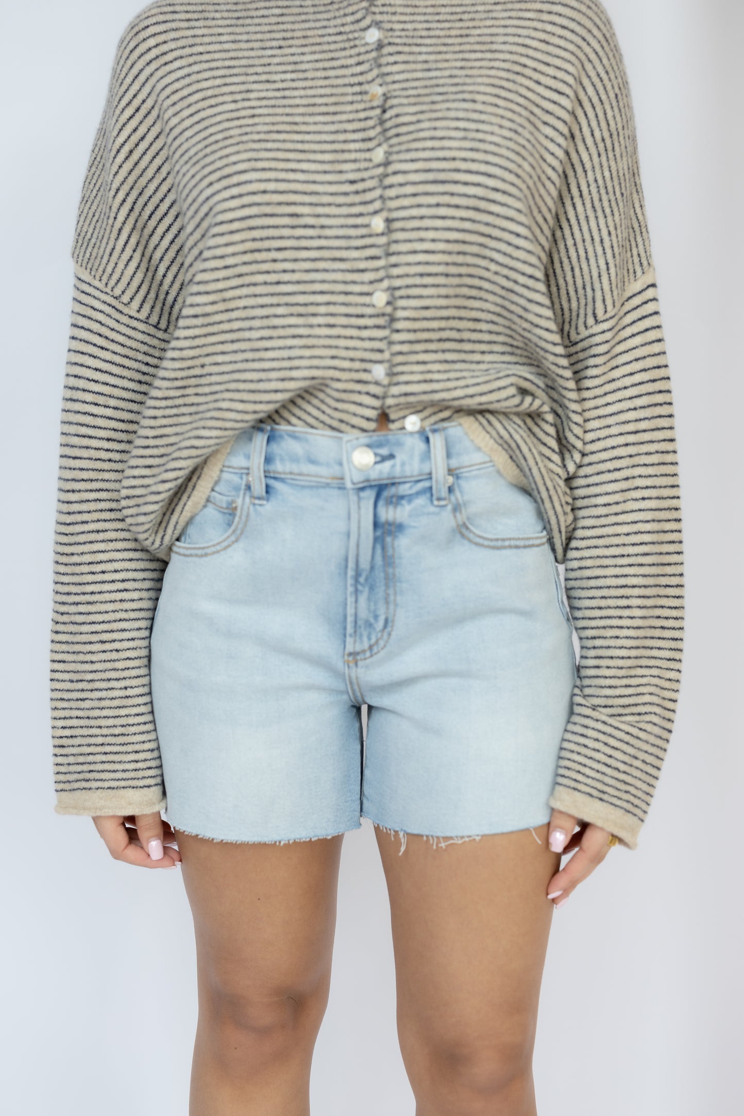 Person wearing a striped sweater and light blue denim shorts on a plain background