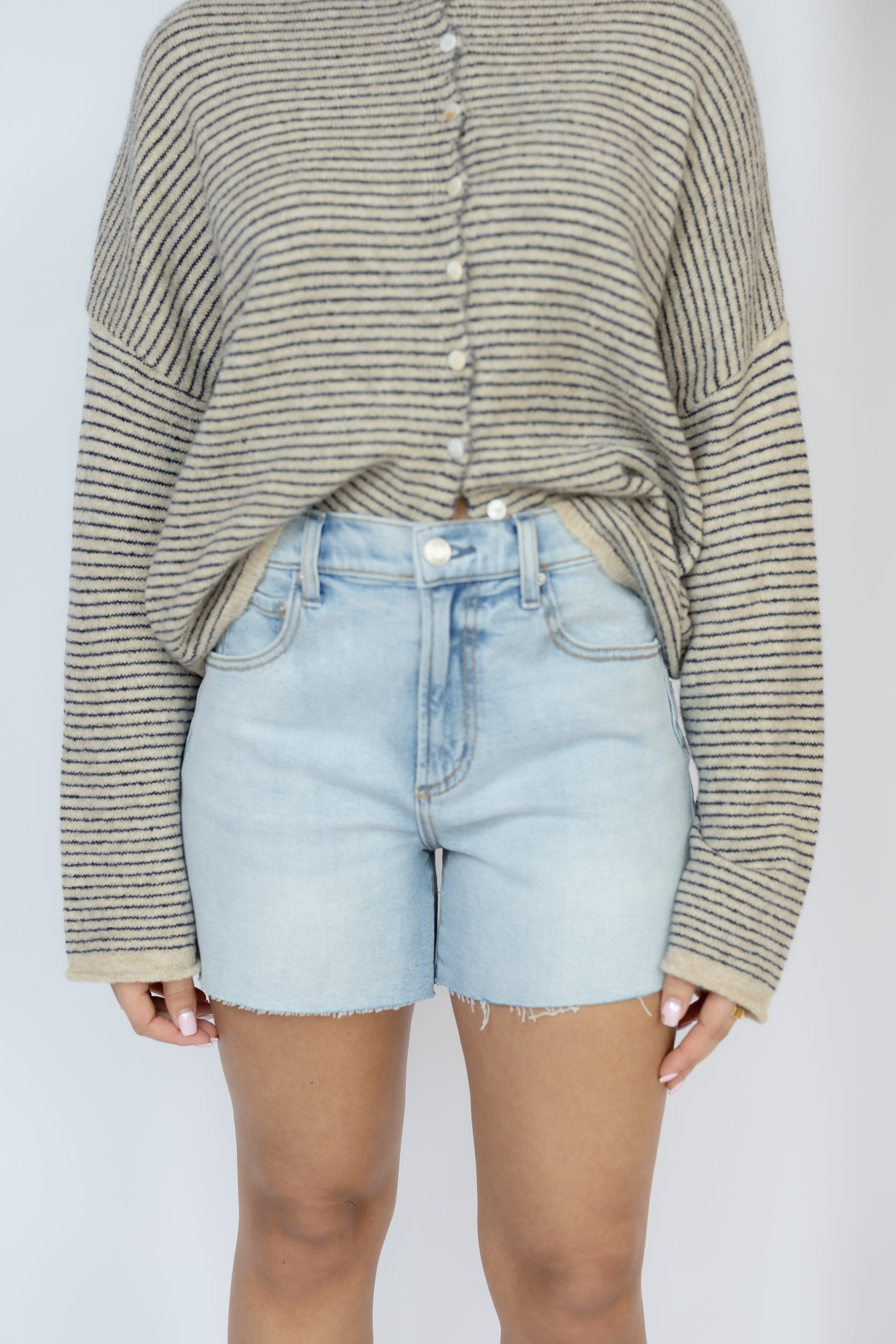 Person wearing a striped sweater and light blue denim shorts on a plain background