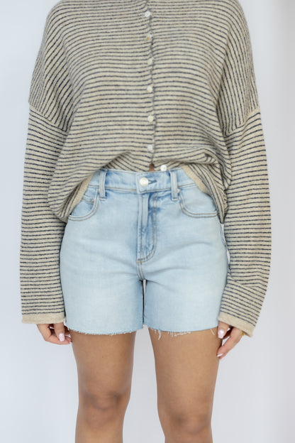 Person wearing a striped sweater and light blue denim shorts on a plain background