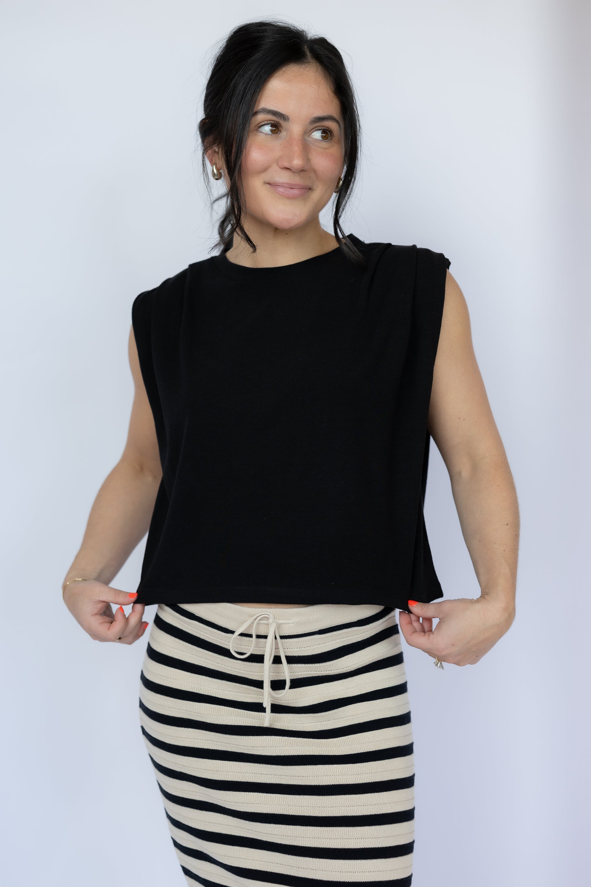 Woman wearing a black sleeveless top and striped skirt against a white background