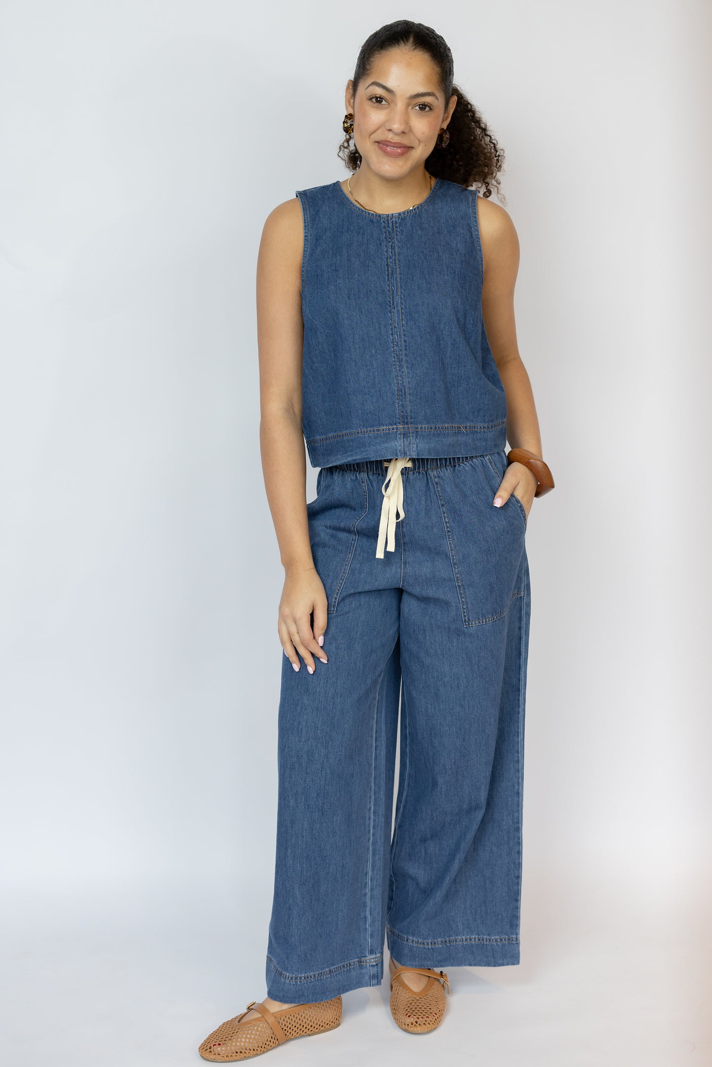 Woman wearing a blue denim sleeveless top and wide-leg pants on a white background