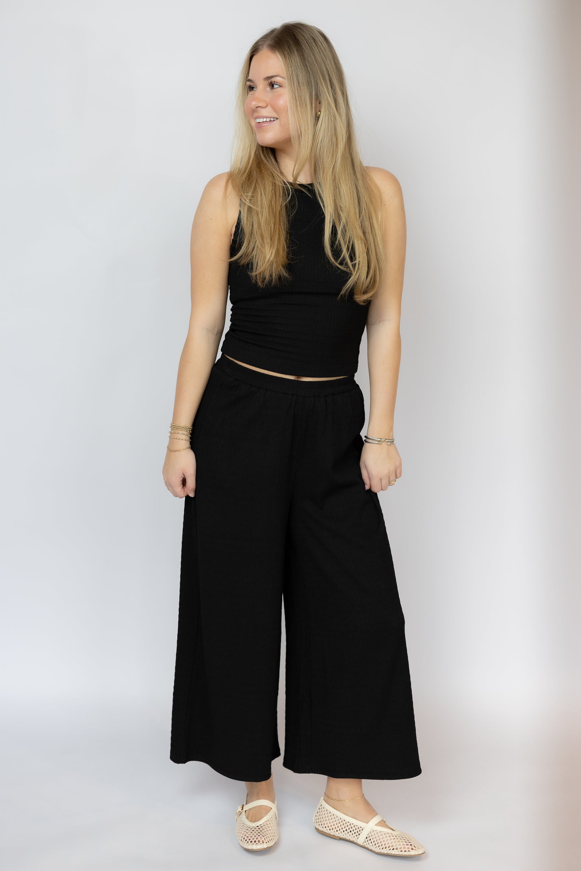 Woman wearing a black sleeveless top and wide-leg pants against a white background