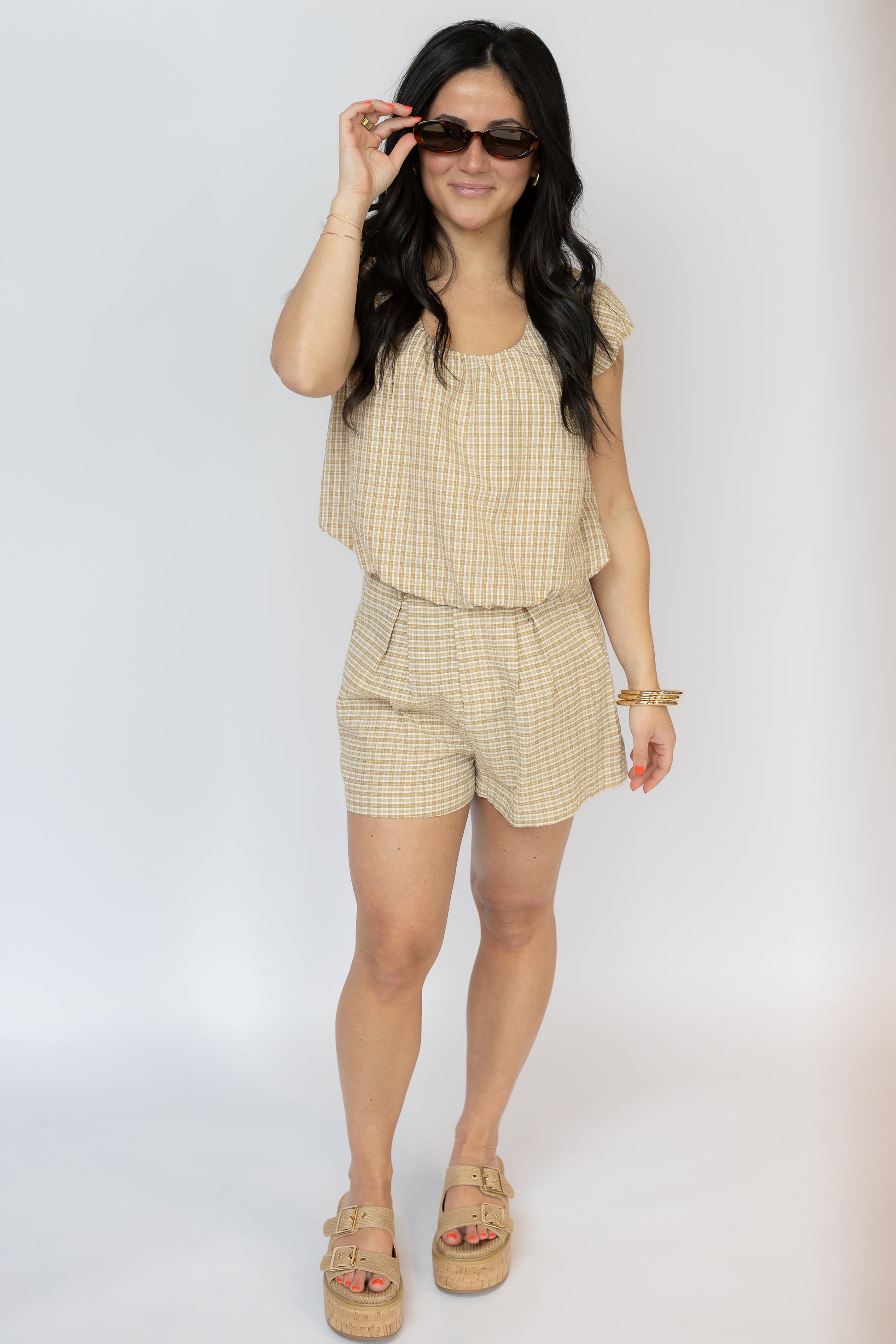 Woman wearing a beige checkered outfit with sunglasses on a white background