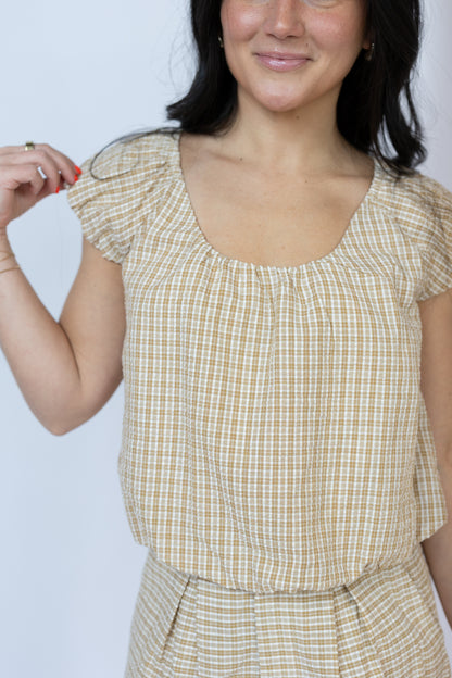 Woman wearing a yellow checkered top and skirt against a light blue background