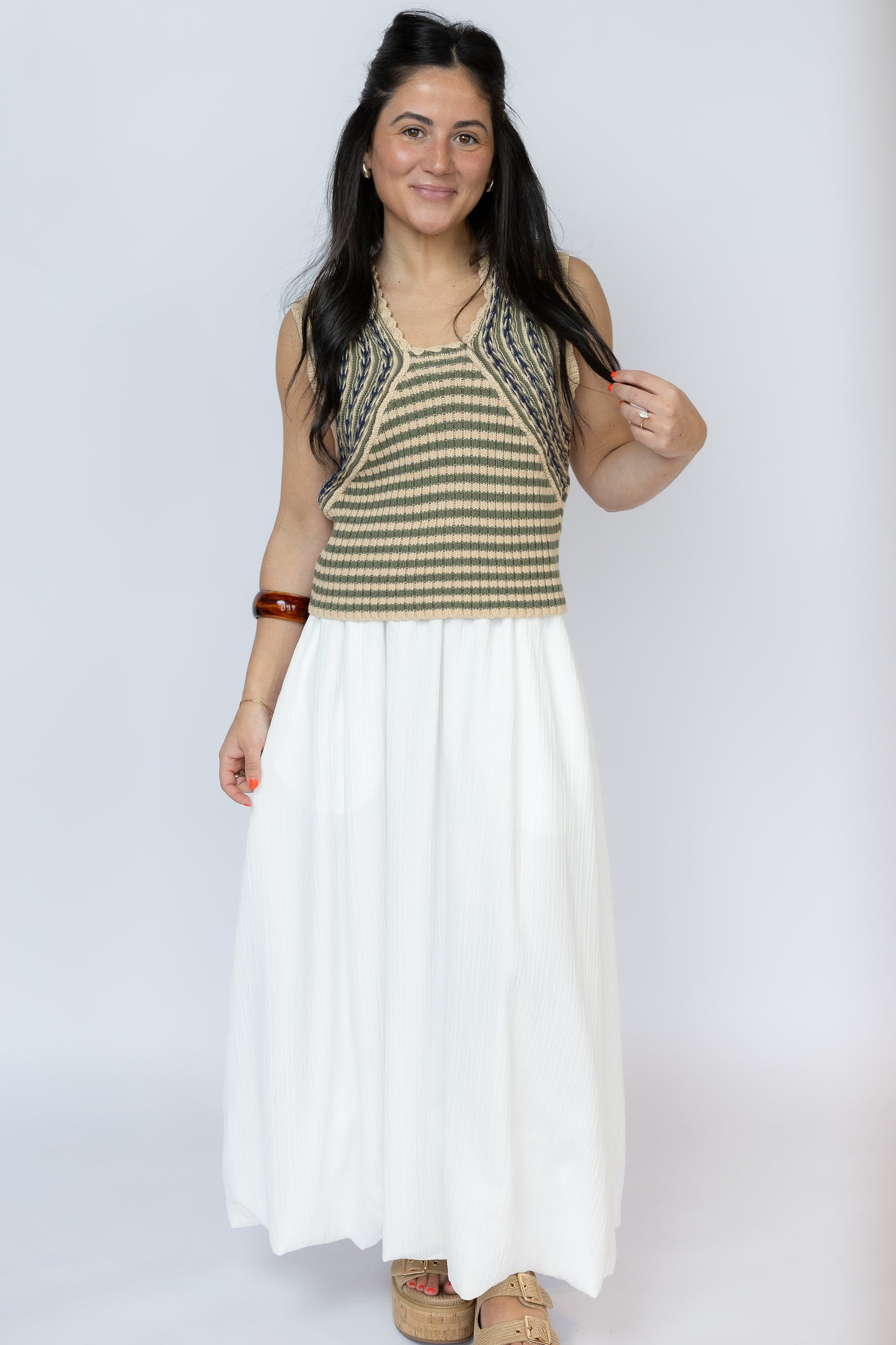 Woman wearing a sleeveless striped top and white skirt on a plain background