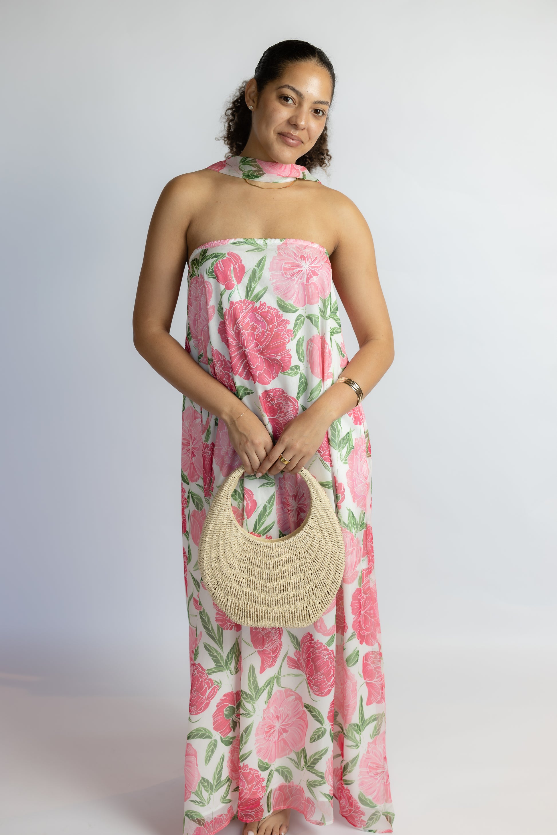 Woman wearing a floral dress holding a woven bag against a white background