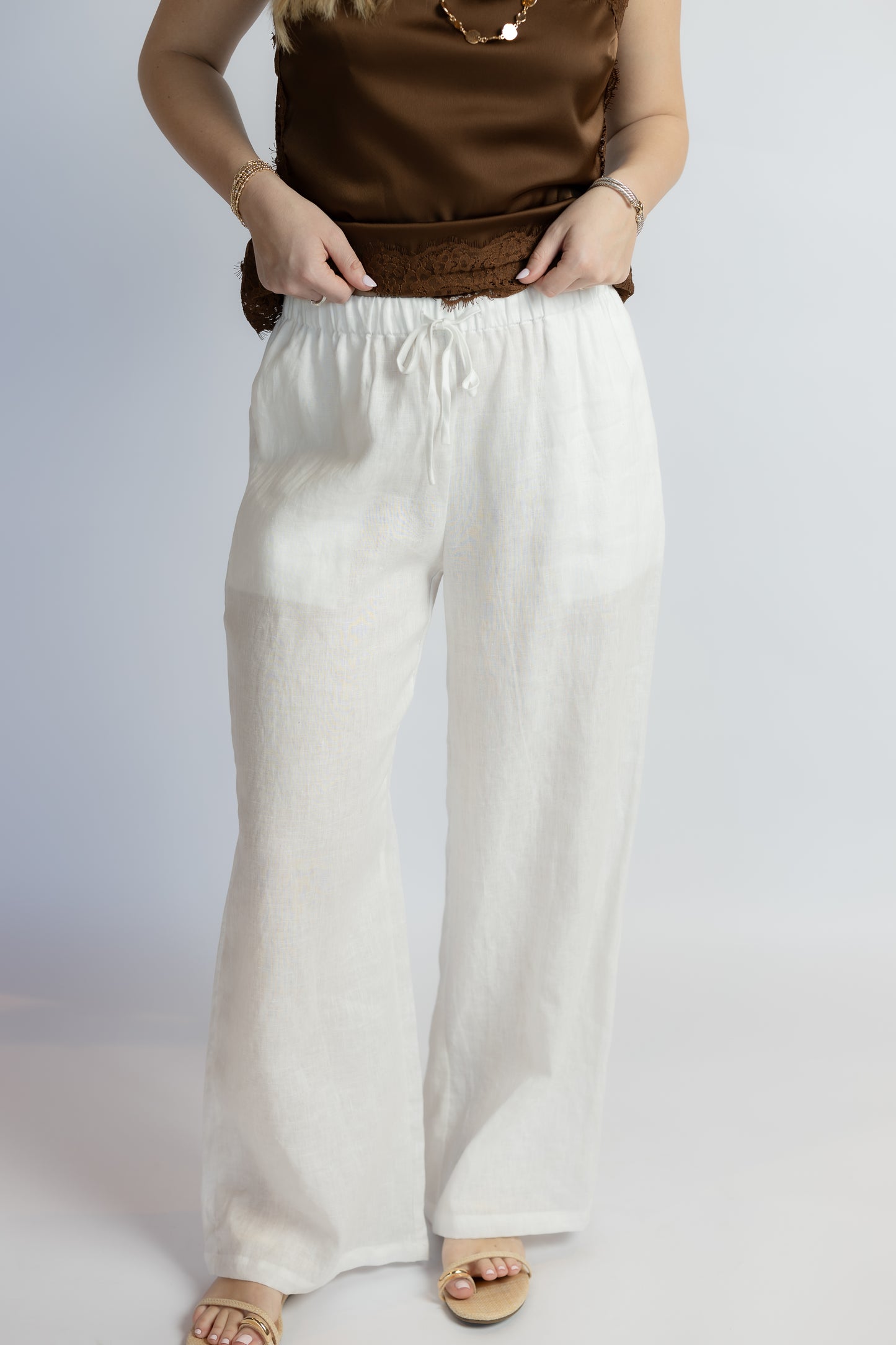 Person wearing a brown top and white linen pants on a plain background