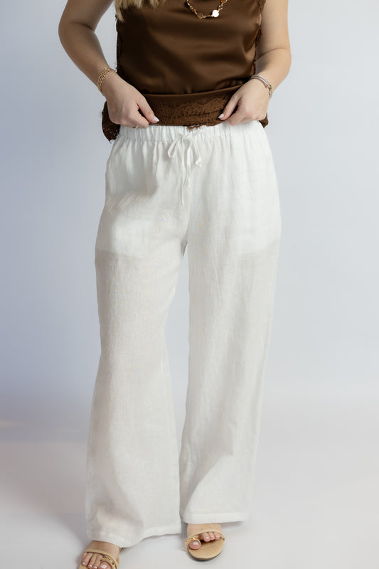 Person wearing a brown top and white linen pants on a plain background