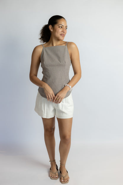 Woman wearing a beige sleeveless top and white shorts on a plain background