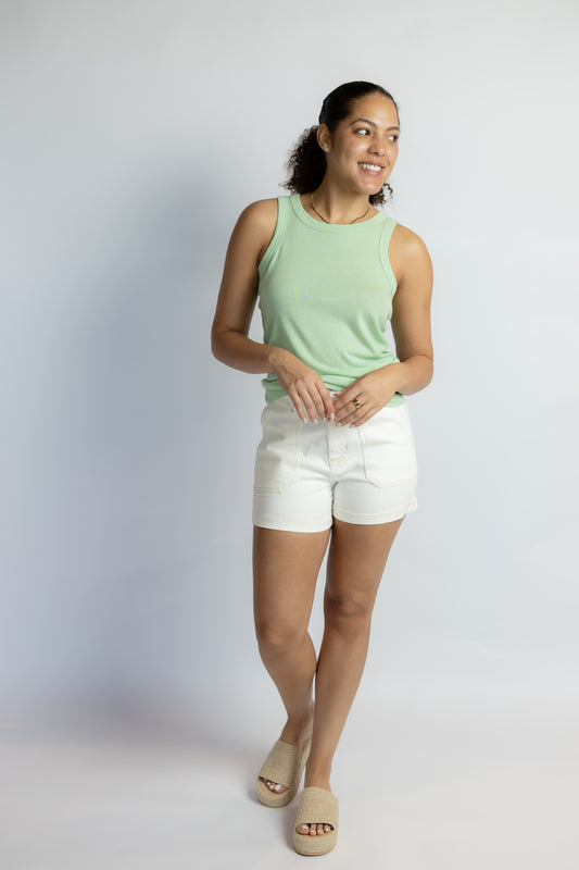 Woman wearing a light green sleeveless top and white shorts on a plain background