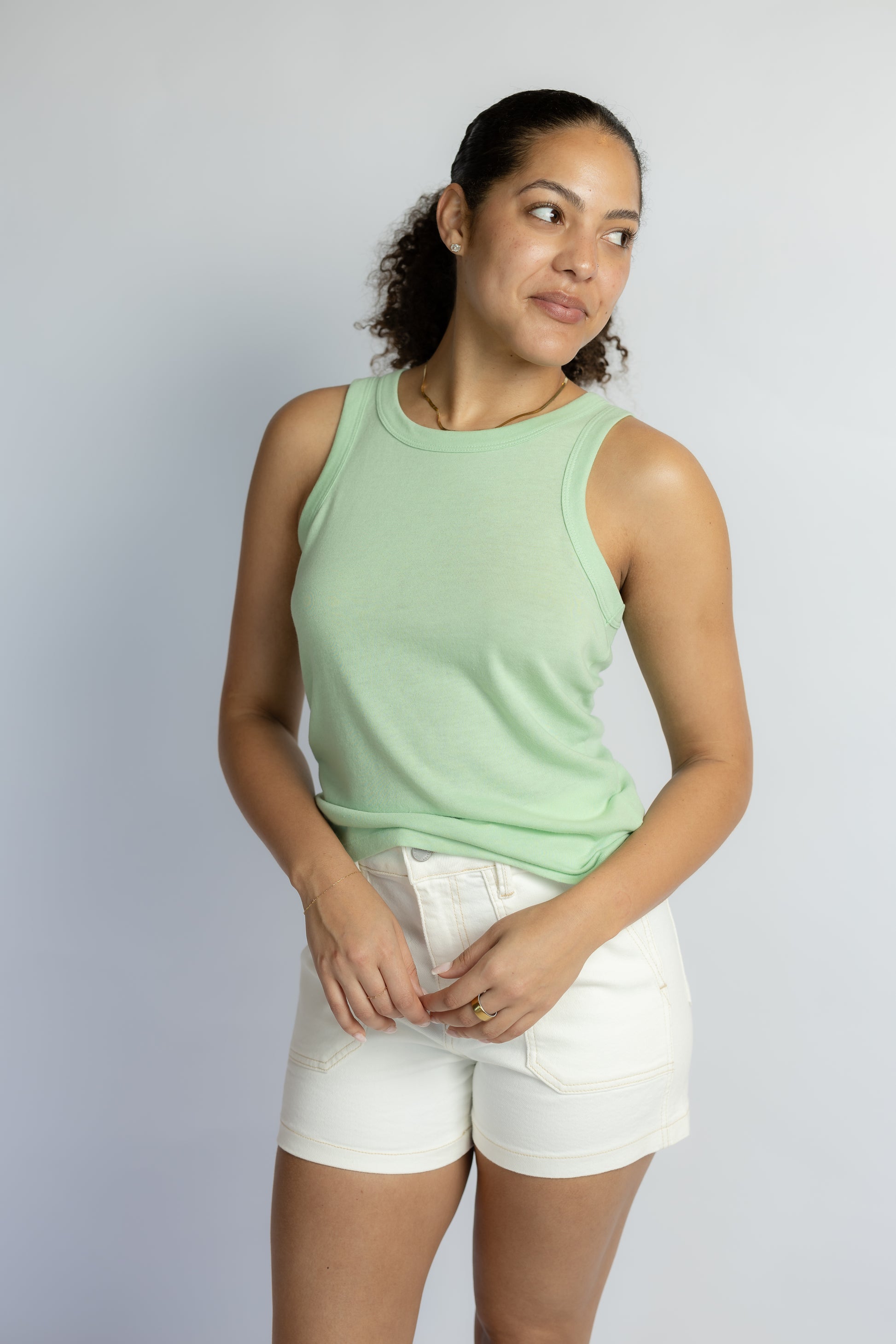 Woman wearing a light green sleeveless top and white shorts against a plain background