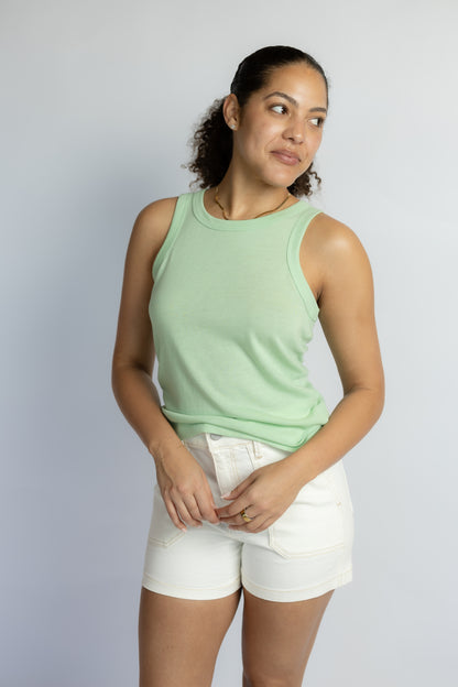 Woman wearing a light green sleeveless top and white shorts against a plain background