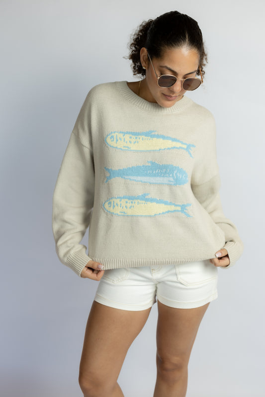 Woman wearing a light-colored sweater with fish designs and white shorts on a plain background