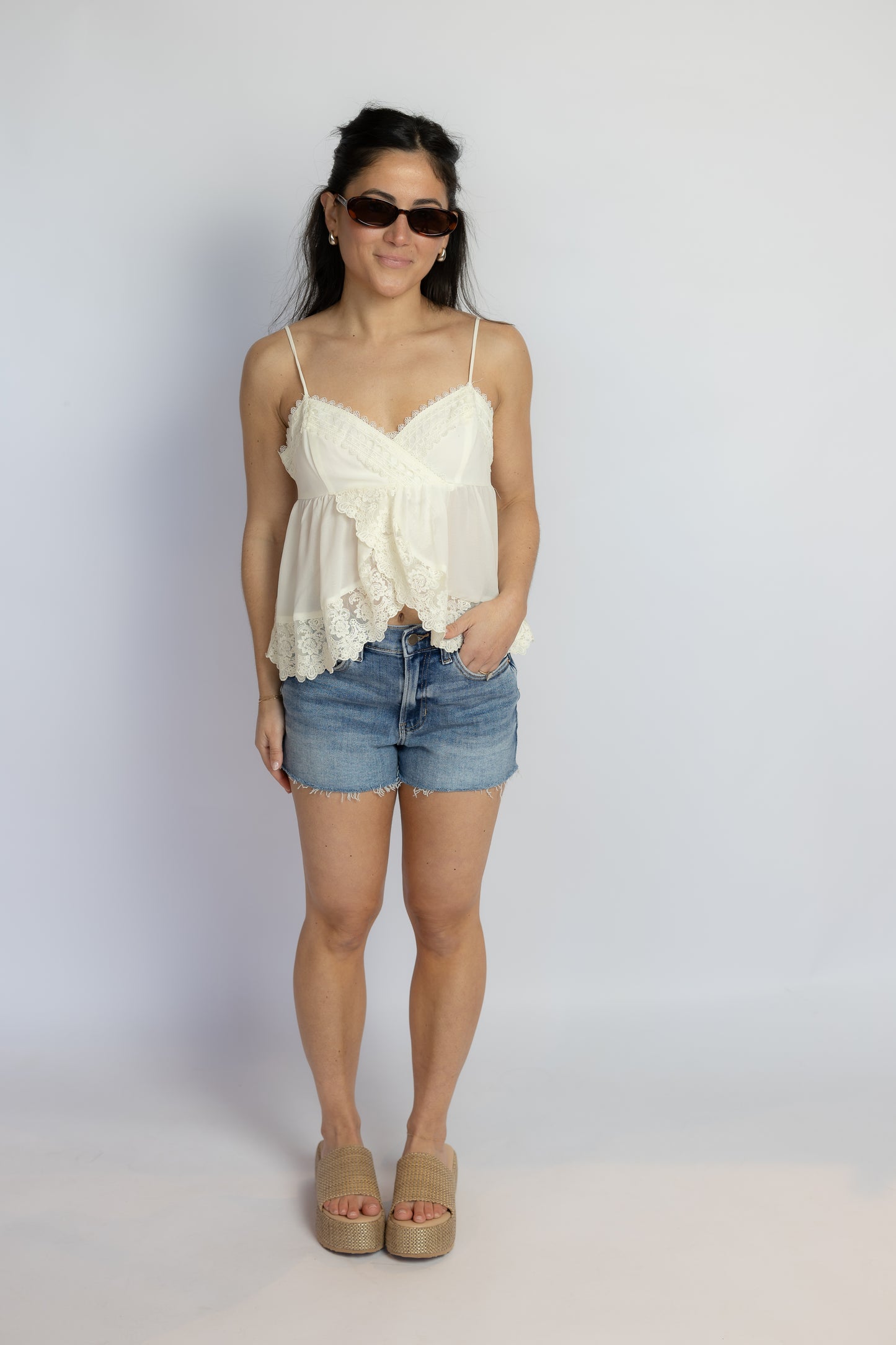 Woman wearing a white lace top and denim shorts against a plain background