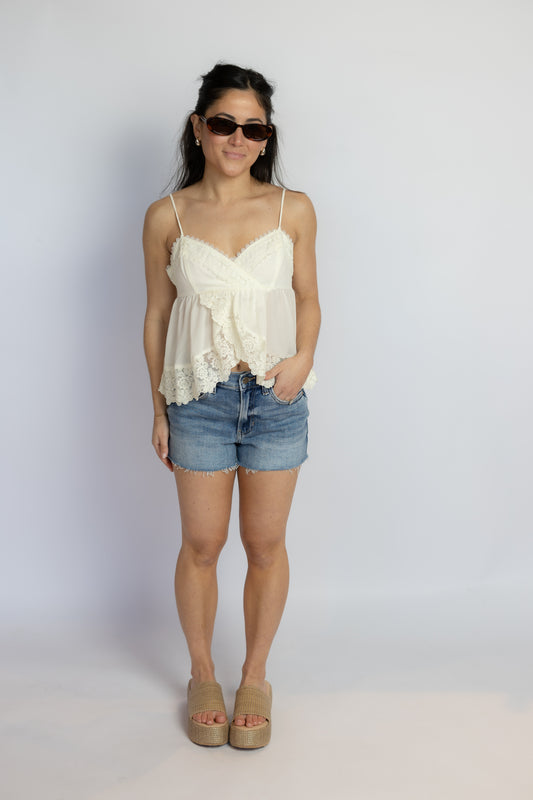 Woman wearing a white lace top and denim shorts against a plain background