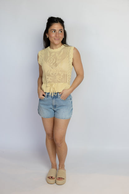 Woman wearing a yellow sleeveless top and denim shorts against a white background