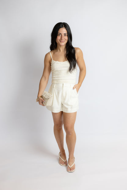 Woman wearing a white top and linen shorts standing against a plain background