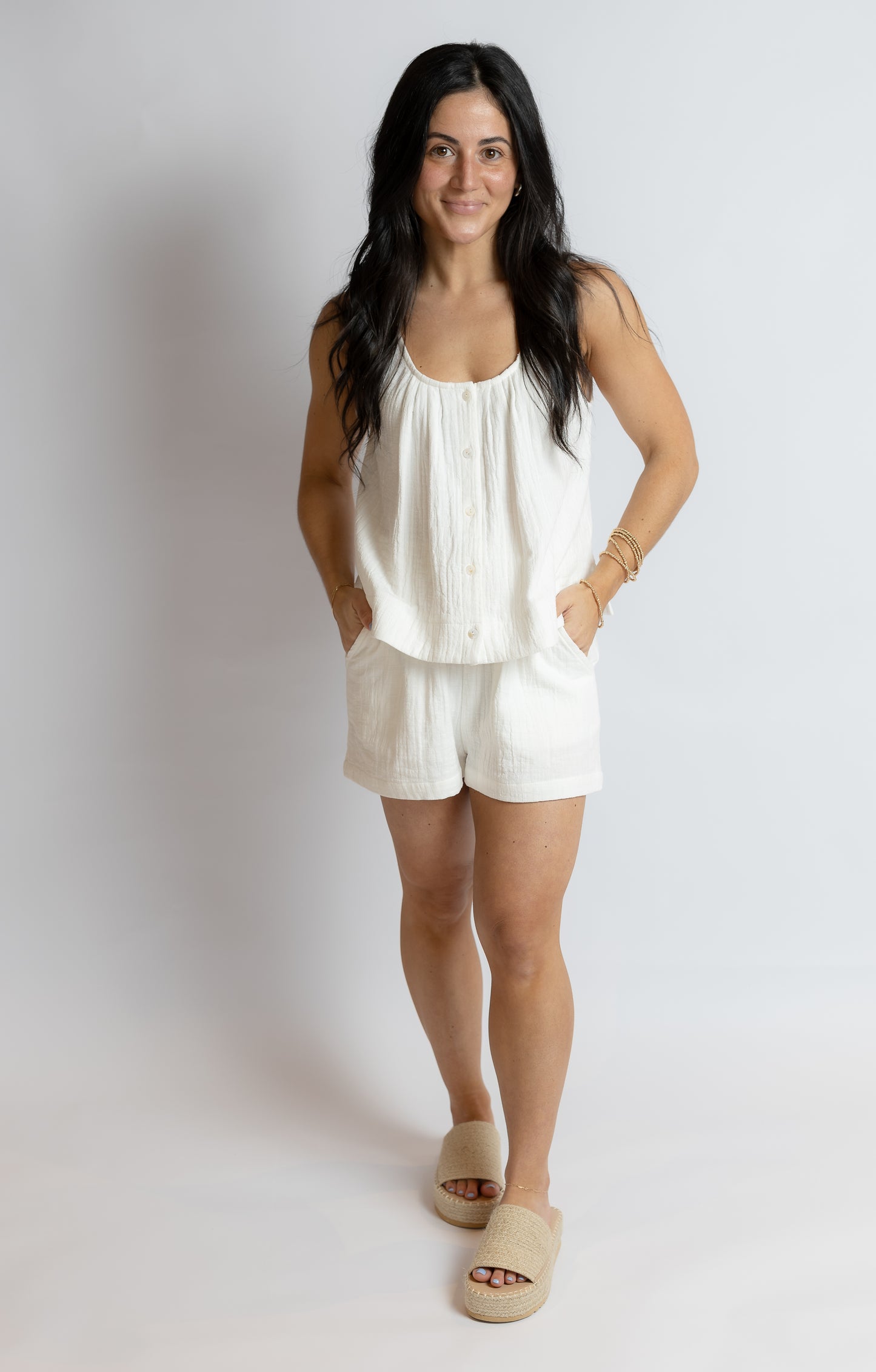 Woman wearing a white sleeveless top and shorts on a plain background