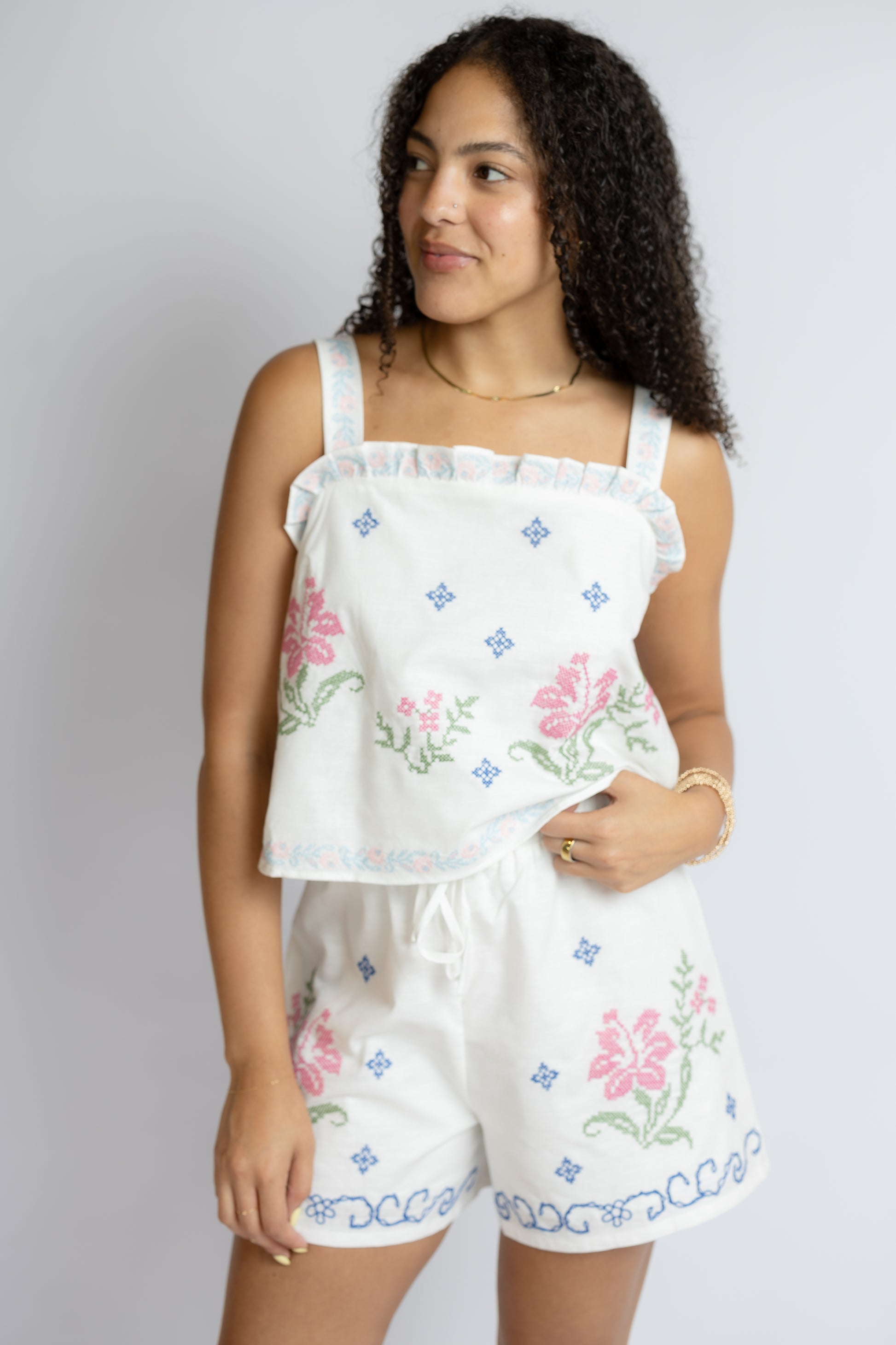 Woman wearing a white embroidered top and shorts set against a plain background