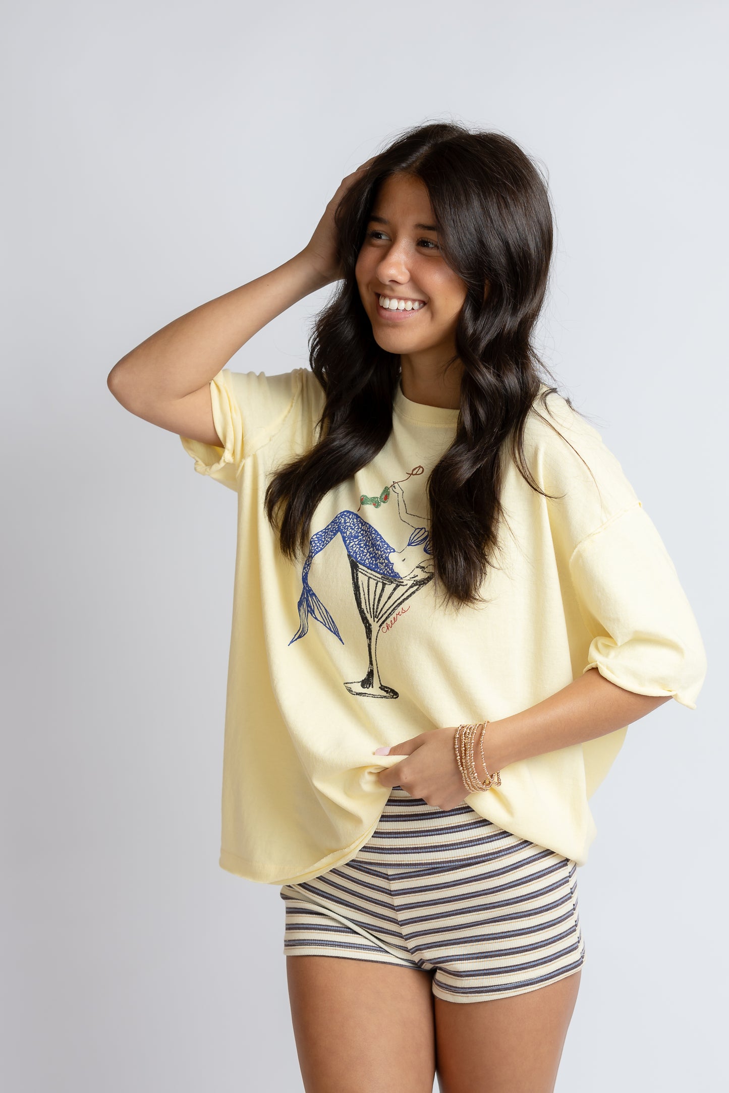 Woman wearing a yellow oversized t-shirt with a graphic design and striped shorts on a plain background