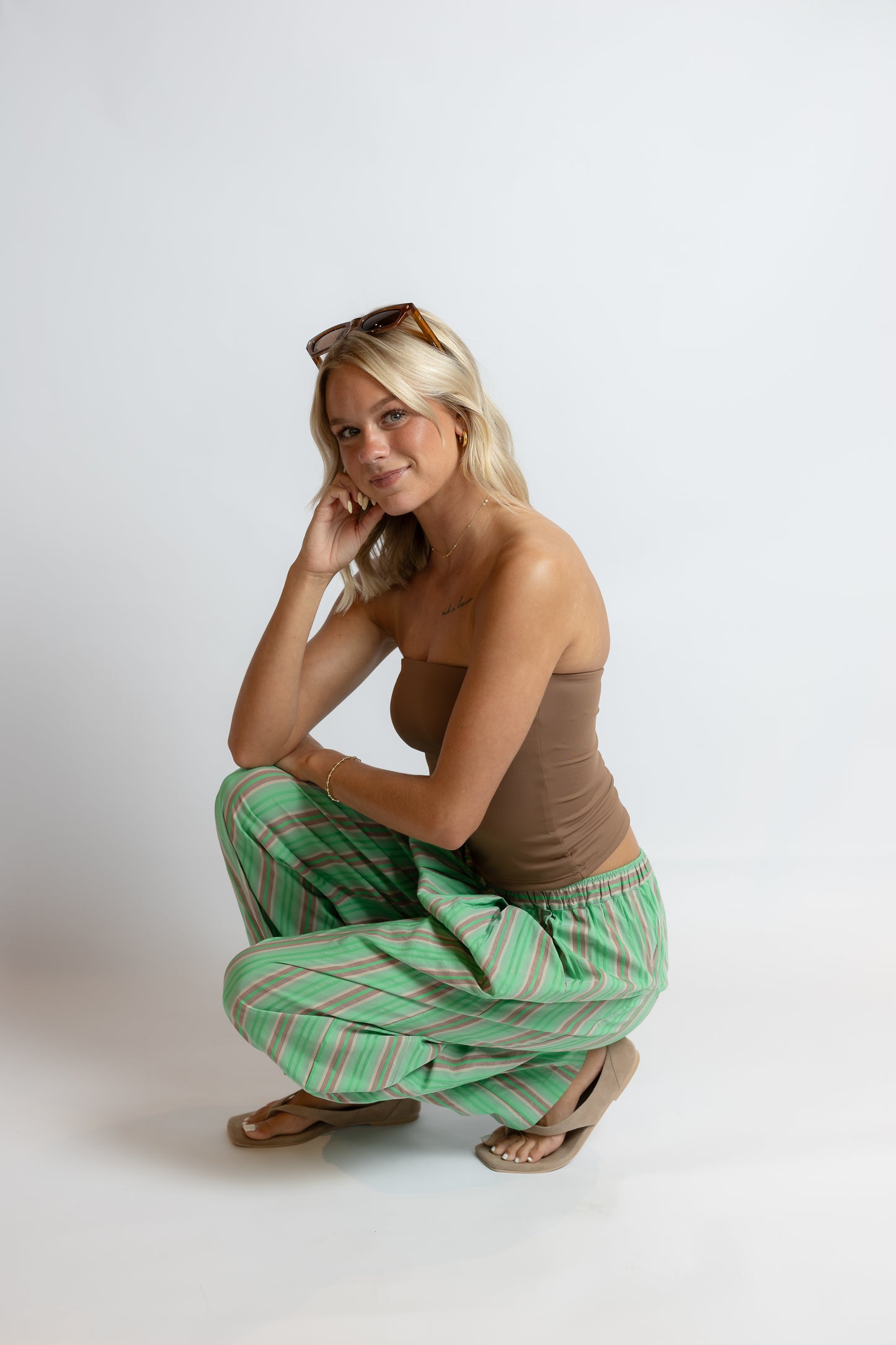 Woman wearing a brown top and green striped pants posing against a white background