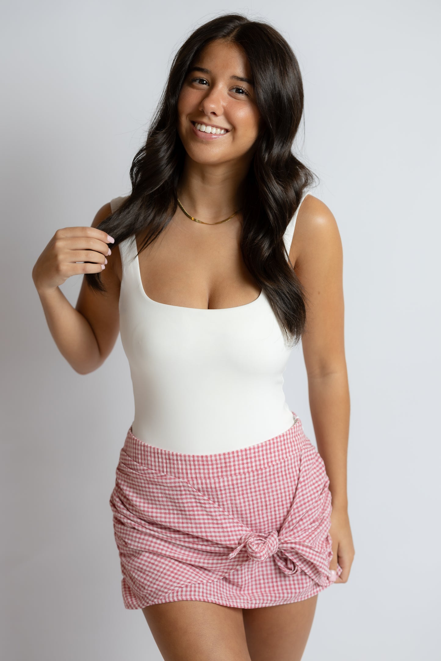 Woman wearing a white tank top and red checkered skirt on a plain background