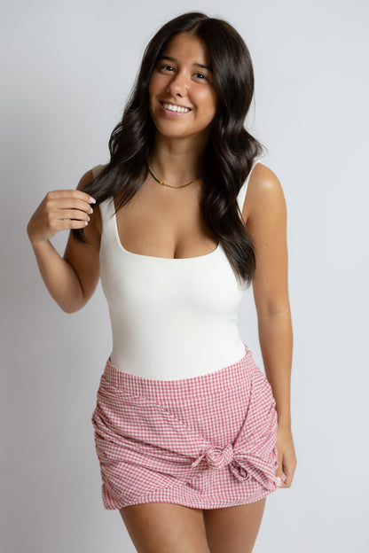 Woman wearing a white tank top and red checkered skirt on a plain background