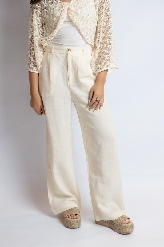 Person wearing a beige lace top, white pants, and beige shoes on a plain background