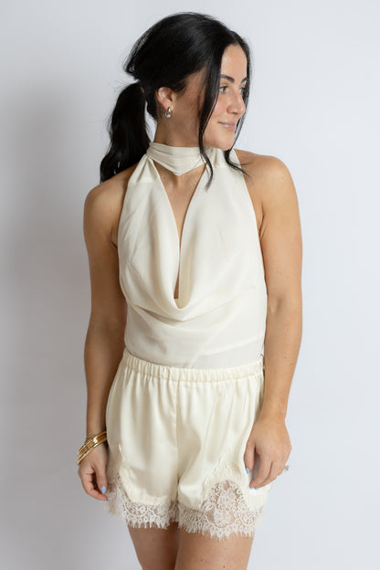 Woman wearing a cream-colored outfit with lace details on a plain background