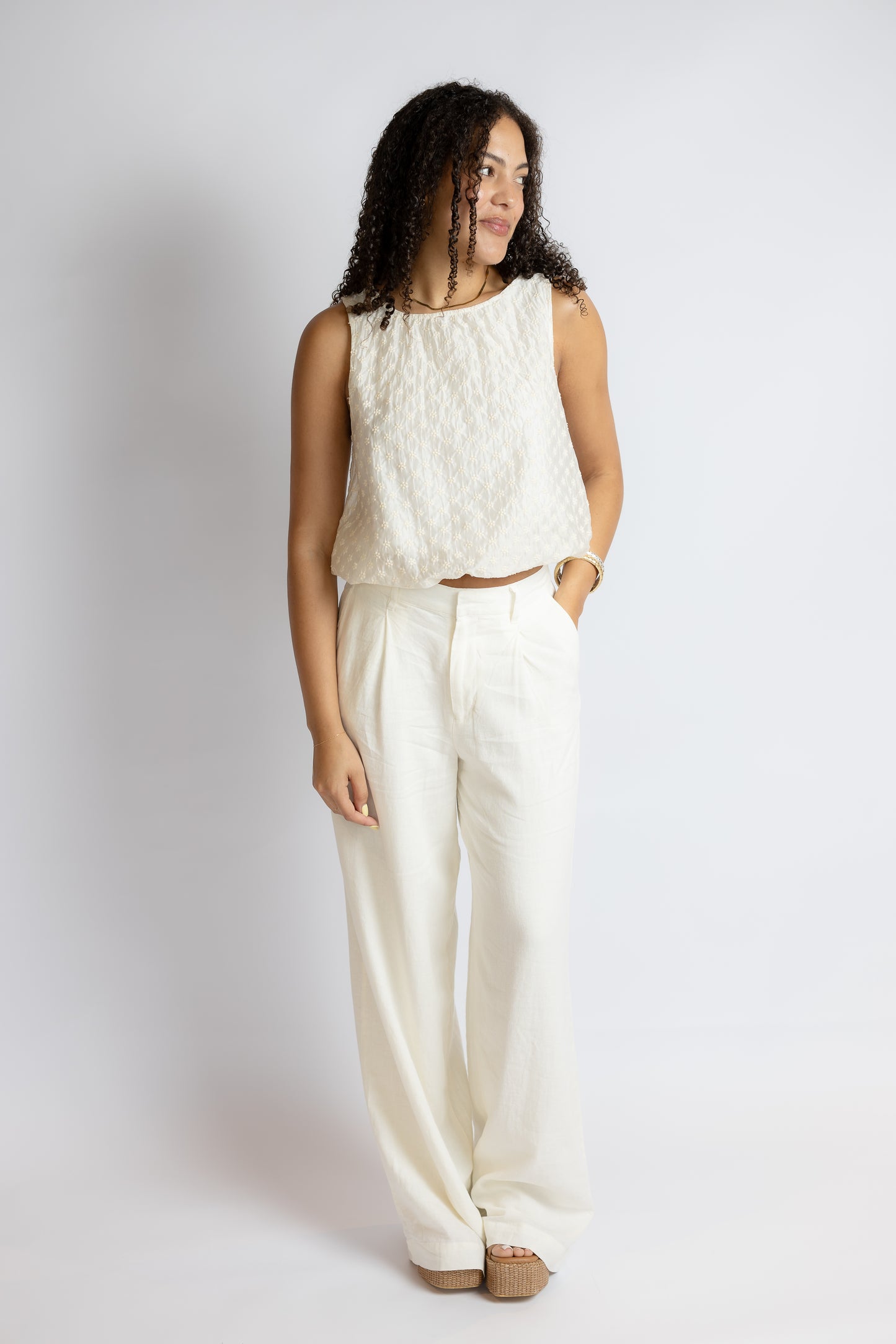 Woman wearing a white sleeveless top and pants against a plain background