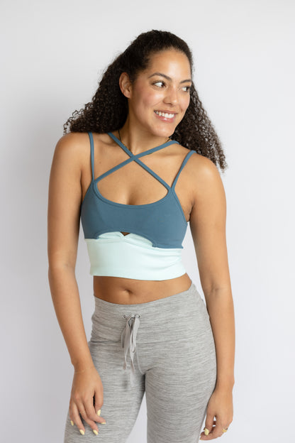 Woman wearing a blue sports bra and gray leggings on a white background