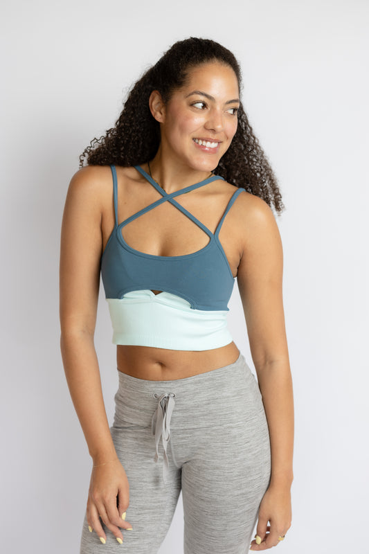 Woman wearing a blue sports bra and gray leggings on a white background