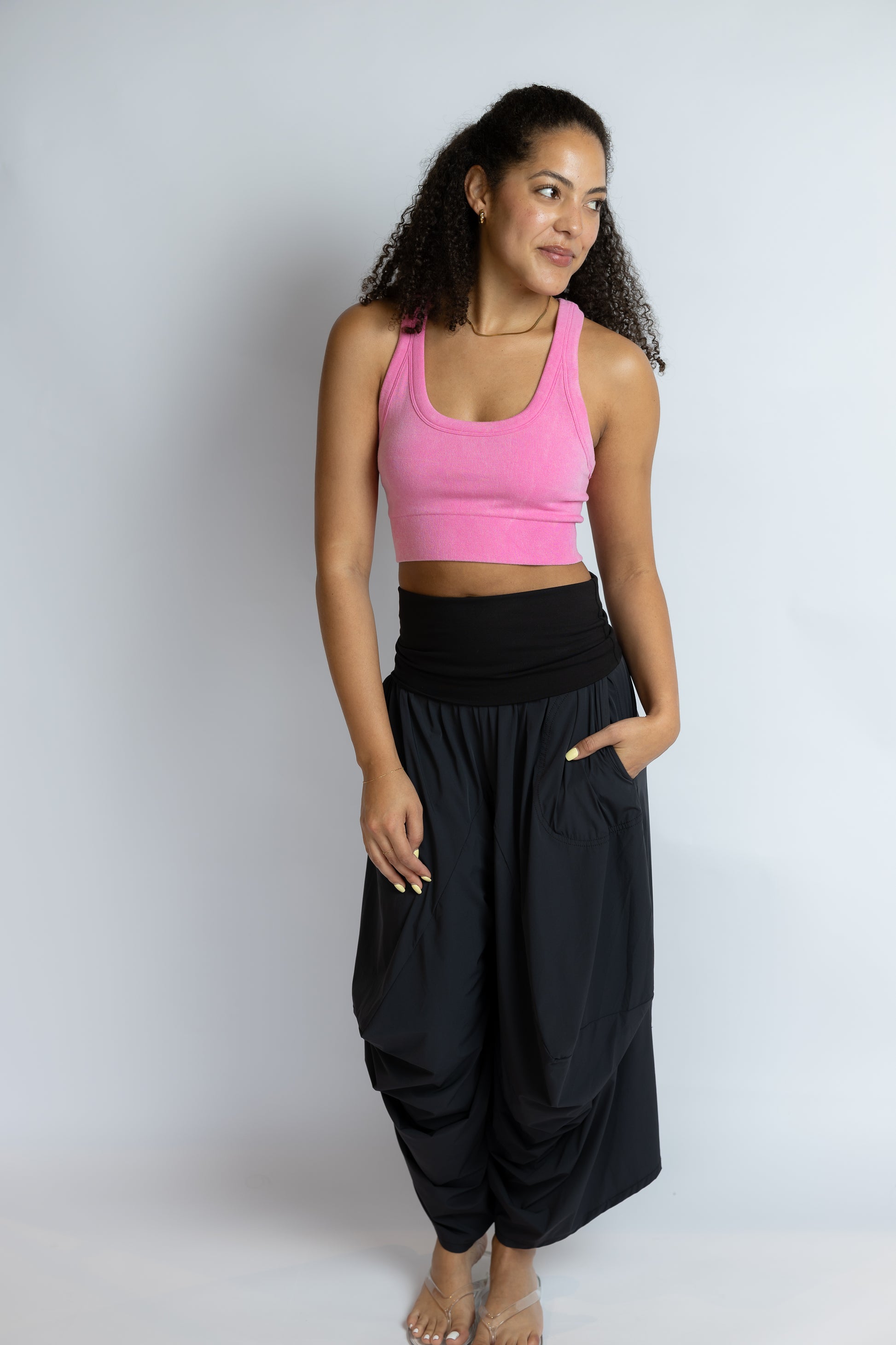 Woman wearing a pink top and black pants against a white background