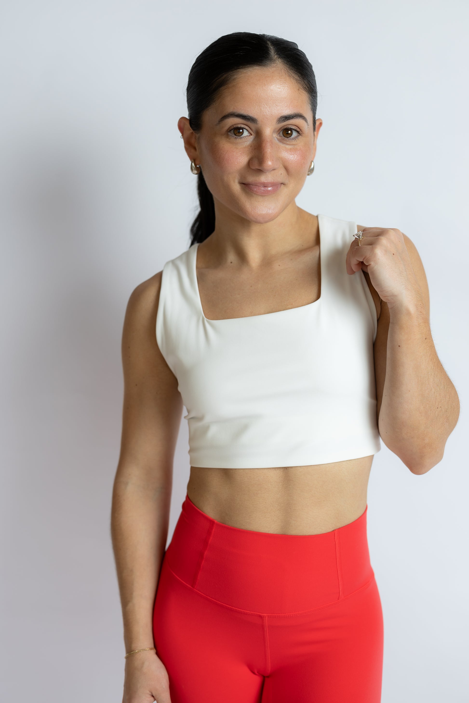 Woman wearing a white crop top and red leggings against a plain background
