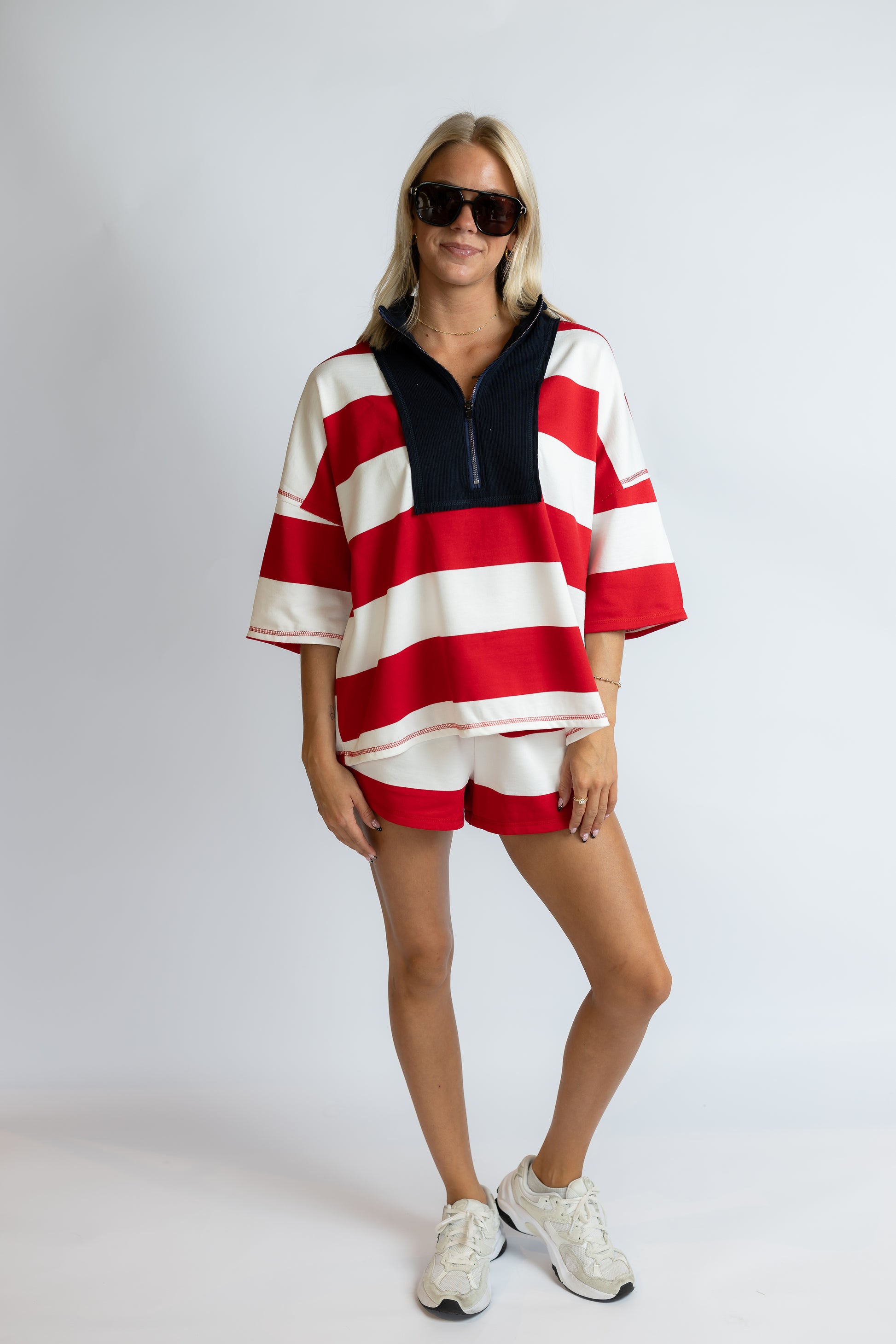 Woman wearing a red and white striped outfit with sunglasses on a plain background
