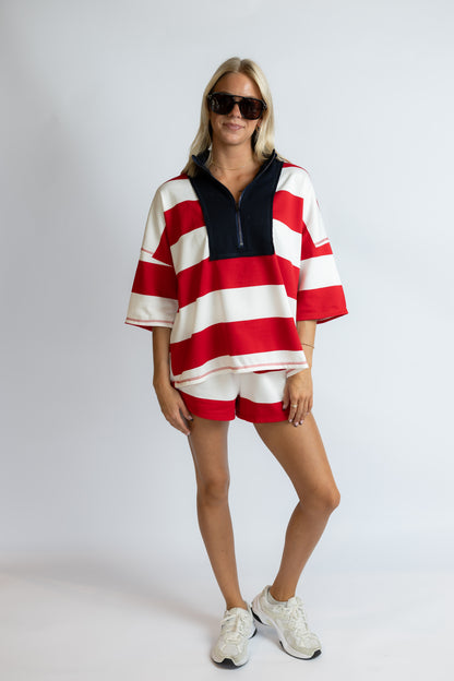 Woman wearing a red and white striped outfit with sunglasses on a plain background